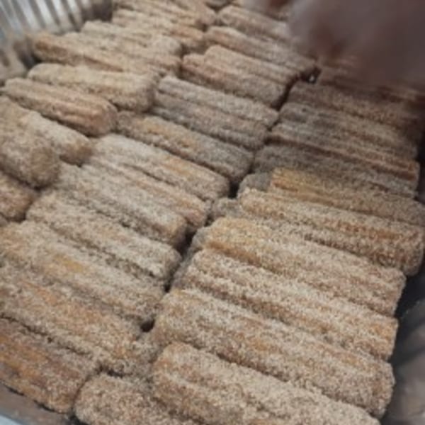 Rows of freshly made churros, coated in cinnamon sugar, fill a metal tray.