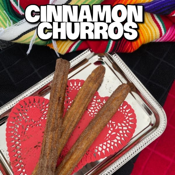 Cinnamon churros on a silver tray with red heart-shaped doilies, against a colorful striped fabric.