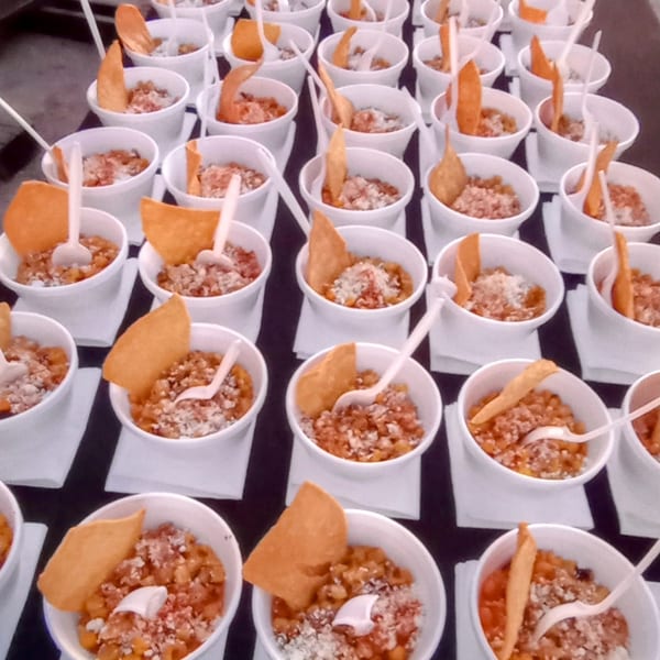 Rows of small white cups filled with a savory dish, topped with a chip and a spoon.
