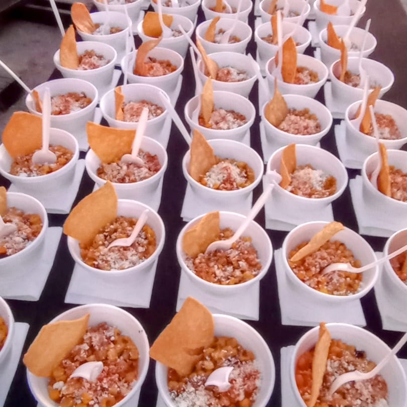 Rows of small white cups filled with a savory dish, topped with a chip and a spoon.