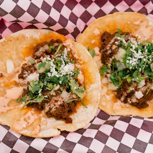 Two delicious tacos with meat, cilantro, onions, and sauce on a checkered paper.