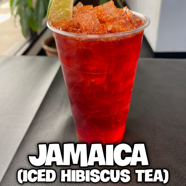 Jamaica iced hibiscus tea with a lime wedge and chili powder on a dark surface.