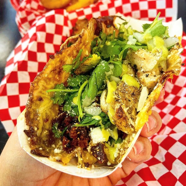 A hand holds a Blacktop Grill street taco filled with meat, cheese, cilantro, and sauce.