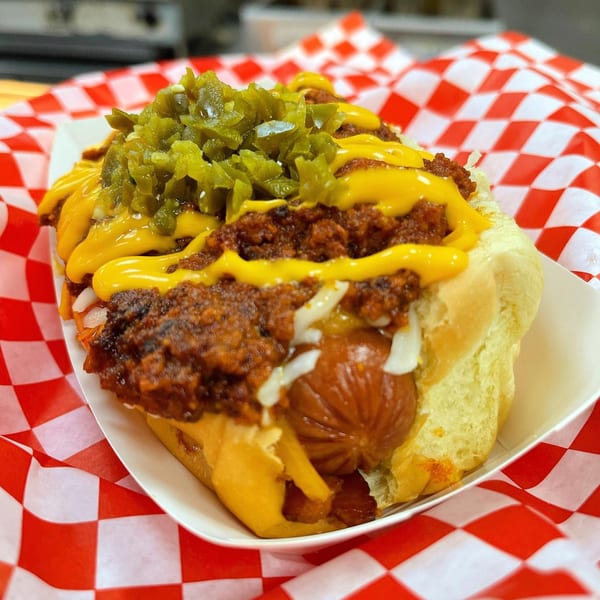 A chili cheese hot dog from The Blacktop Grill, topped with diced jalapeños, in a paper tray.