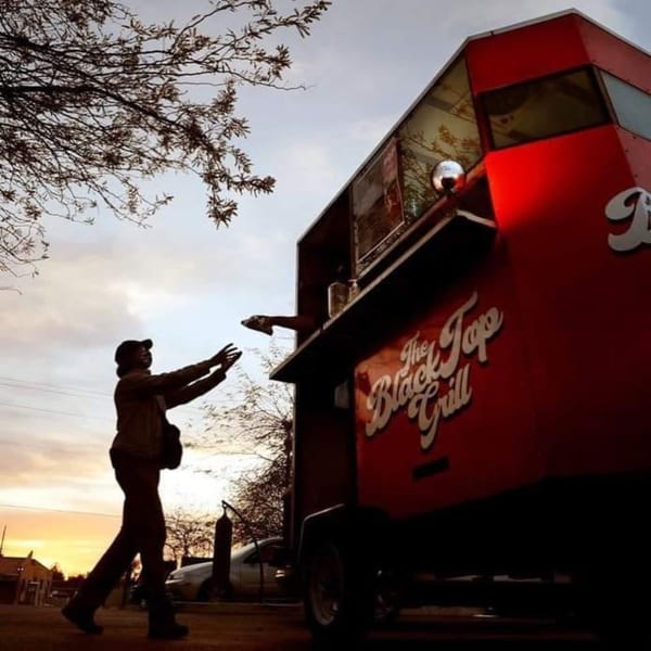 A person reaches for food from The Black Top Grill food truck at sunset.